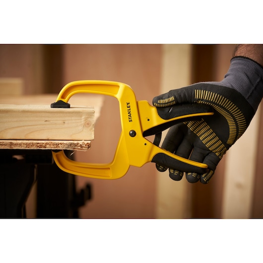 STANLEY STHT0-83200 klem houdt houten planken vast, gehandschoende hand bedient, product in werkplaats.