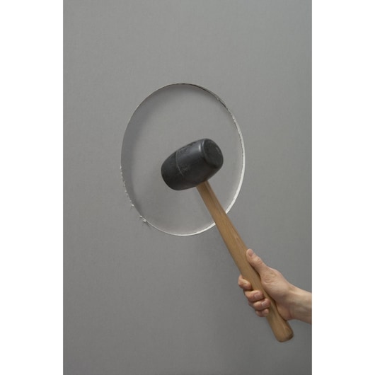 STANLEY STHT1-05878 rubberen hamer met houten handvat, zijaanzicht, tegen een grijze muur met ronde uitsparing gehouden.