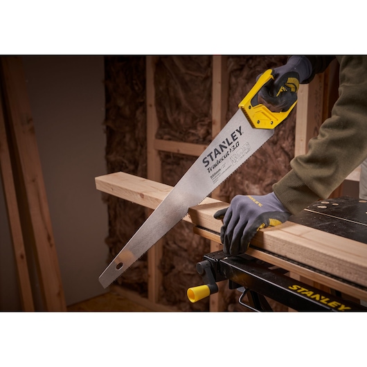 STANLEY STHT1-20352 scie à main à poignée jaune coupant une poutre en bois dans un atelier.