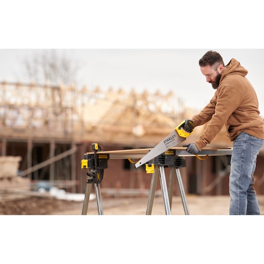 STANLEY STHT1-20352 scie à main utilisée à l’extérieur sur un chantier, coupe du bois sur un établi.