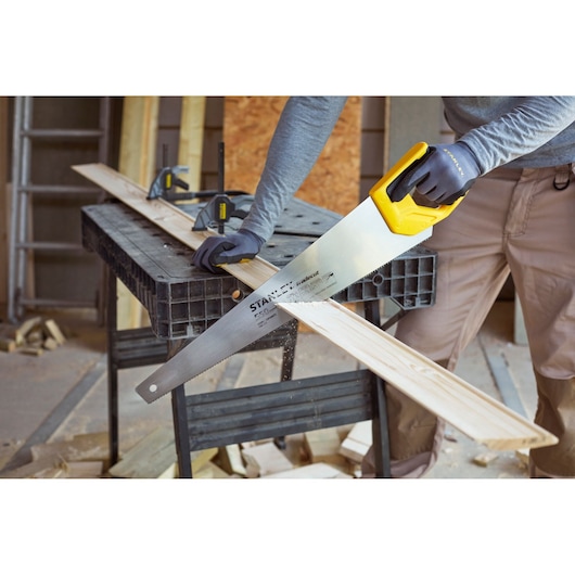STANLEY STHT1-20353 handzaag met gele handgreep zaagt houten plank in werkplaats.