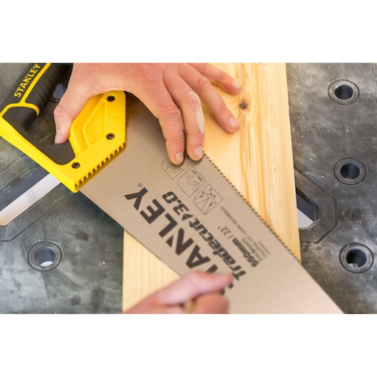 STANLEY STHT1-20353 handzaag met gele handgreep zaagt houten plank op werkbank.
