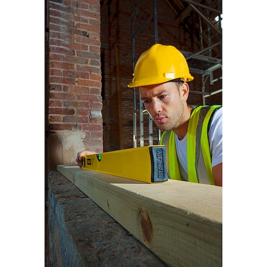 Foto van STANLEY STHT1-43102 waterpas in gebruik op houten balk op bouwplaats.