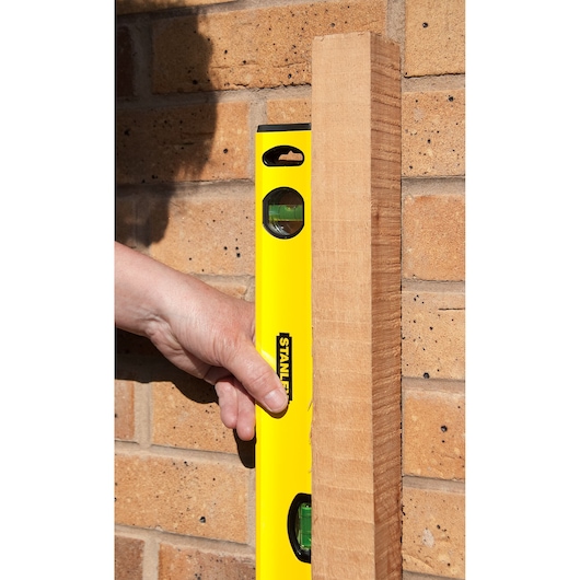 STANLEY STHT1-43103 gele waterpas tegen hout en bakstenen muur, close-up weergave.