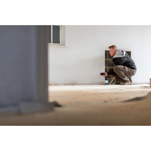 STANLEY STHT1-77139 laserafstandsmeter in gebruik voor het meten van een muur in een kamer tijdens de bouw.
