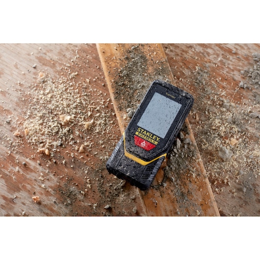 STANLEY STHT1-77139 laser afstandsmeter op stoffig hout, robuust ontwerp, bouwlocatie context.