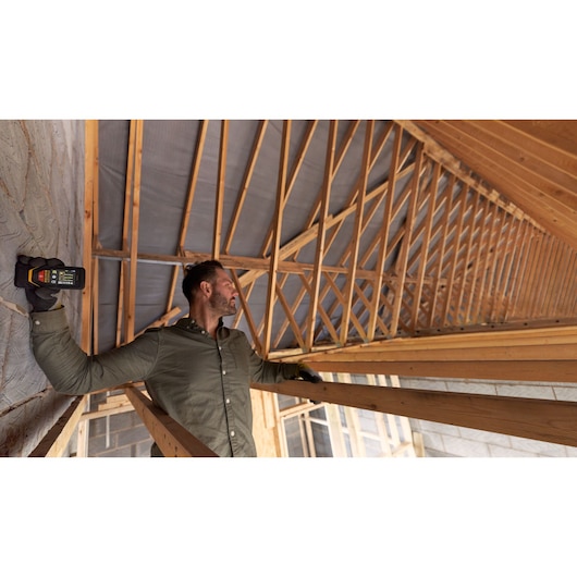 Personne utilisant le télémètre laser STANLEY STHT1-77140 à l'intérieur d'une charpente en bois.