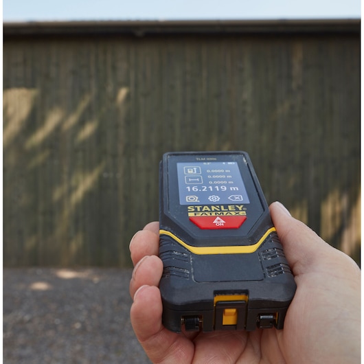 Télémètre laser STANLEY STHT1-77140 tenu en main, écran affichant des mesures, utilisation en extérieur.