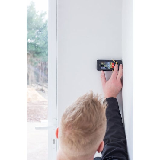 STANLEY STHT1-77140 télémètre laser tenu contre mur blanc par une personne, vue latérale.
