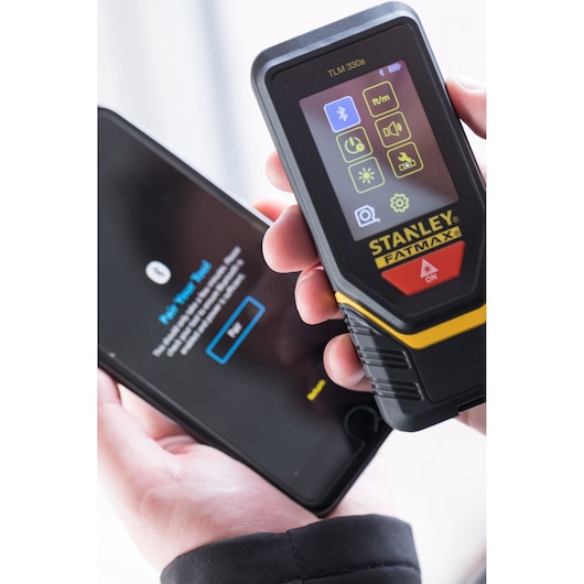 Télémètre laser STANLEY STHT1-77140 tenu près d’un smartphone, vue rapprochée de face.