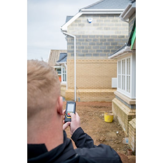 Photographie du télémètre laser STANLEY STHT1-77140 tenu par une personne sur un chantier extérieur.