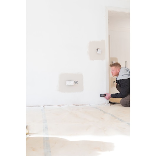 Photo du détecteur mural STANLEY STHT1-77142 en utilisation, personne scannant un mur blanc près d'une prise électrique.