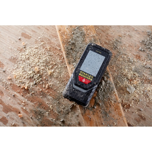 STANLEY STHT1-77142 télémètre laser robuste avec gouttes d'eau sur l'écran, posé sur du bois sale.