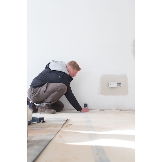 Personne utilisant le télémètre laser STANLEY STHT1-77142 sur un mur dans un chantier.