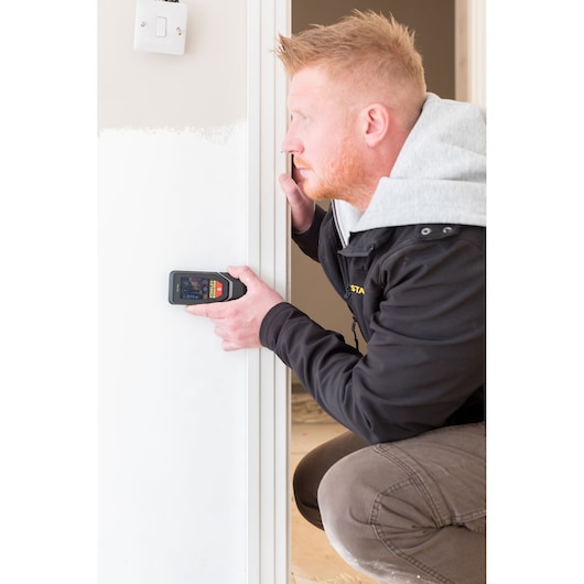 Personne utilisant le détecteur électronique STANLEY STHT1-77142 sur un mur intérieur blanc, vue rapprochée.