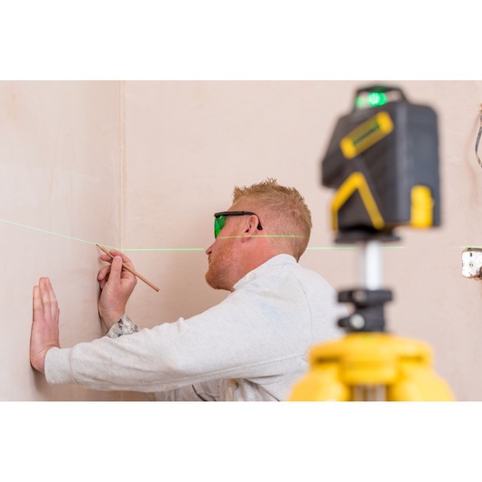 Foto van STANLEY STHT1-77367 laserwaterpas met groene lijn, gebruikt door persoon die muur markeert, categorie fotografie.