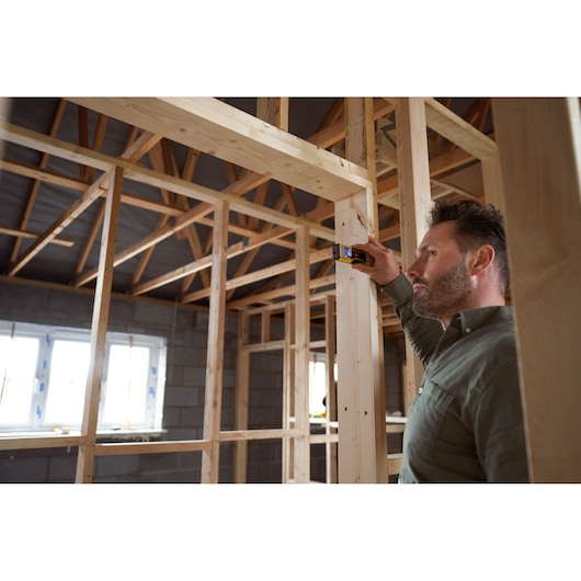 STANLEY STHT1-77409 télémètre laser utilisé par une personne mesurant une ossature en bois dans un bâtiment en construction.