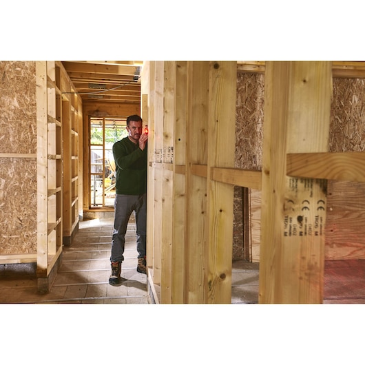 STANLEY STHT1-77409 outil de mesure laser utilisé sur chantier, personne alignant l’outil sur une structure bois.
