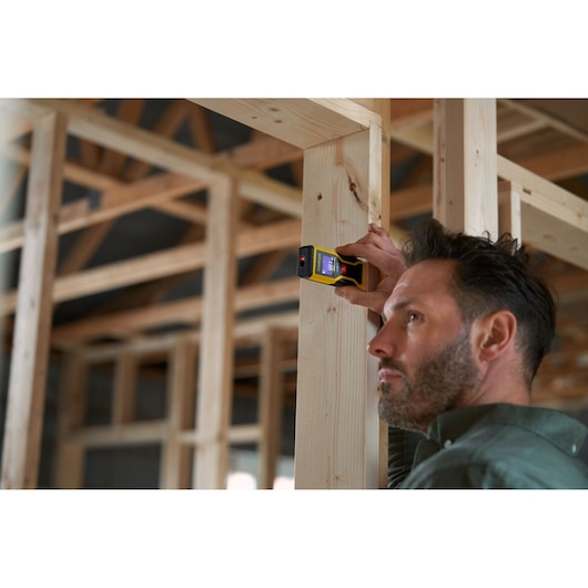 Photo du télémètre laser numérique STANLEY STHT1-77409 utilisé sur une ossature bois, fond de chantier.