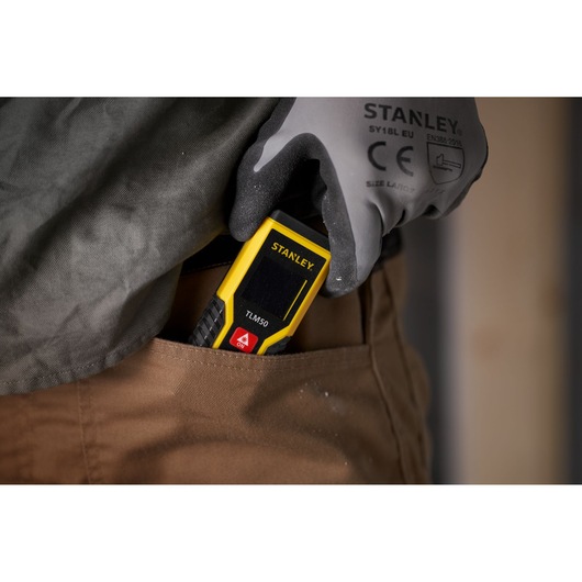 Télémètre laser STANLEY STHT1-77409 TLM50 placé dans une poche de pantalon par une main gantée.