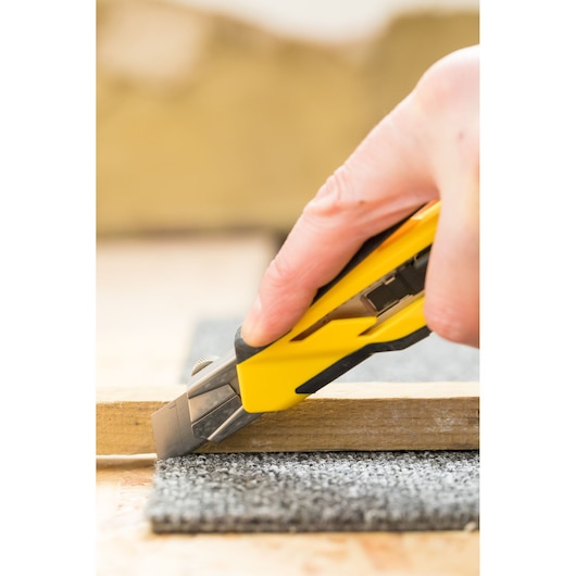 Stanley STHT10270-0 stanleymes snijdt grijs tapijt, close-upfoto van product in gebruik.