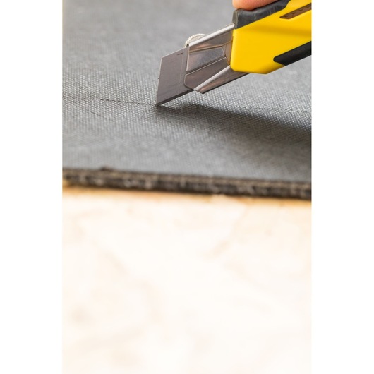 STANLEY STHT10270-0 werkmes snijdt zwart materiaal, close-up, geel met zwart handvat.