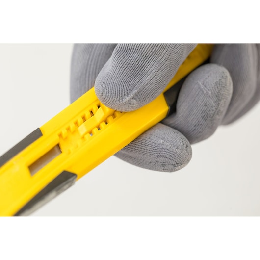Foto van STANLEY STHT10345-0 hobbymes, geel handvat, close-up, vastgehouden door een gehandschoende hand.