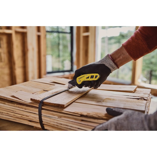 Photo du couteau utilitaire pliant STANLEY STHT10424-0 coupant une sangle en bois sur un chantier.
