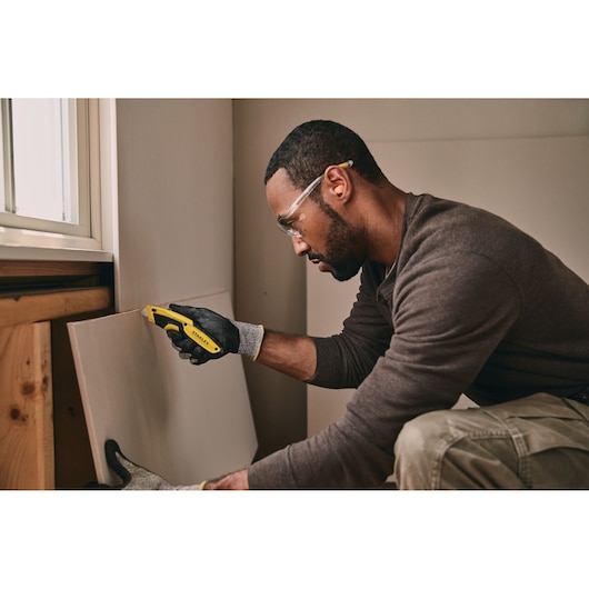 Couteau utilitaire STANLEY STHT10479-0 utilisé pour couper du placoplâtre dans un environnement de chantier.