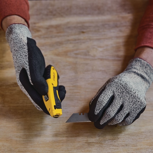 STANLEY STHT10479-0 couteau utilitaire et lame tenus par des mains gantées sur une surface en bois.