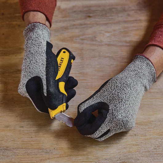 Stanley STHT10479-0 couteau utilitaire tenu avec des gants, changement de lame, vue de table, photographie.