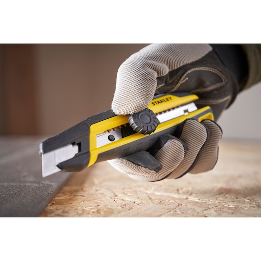 STANLEY STHT10500-0 afbreekmes, geel en zwart, gebruikt door een gehandschoende hand om materiaal te snijden.