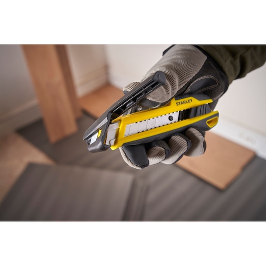 Foto van STANLEY STHT10501-0 hobbymes, geel en zwart, vastgehouden in gehandschoende hand, product close-up.