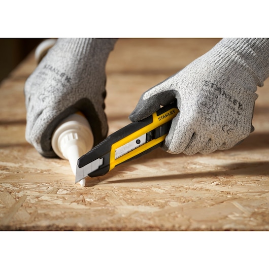 Foto van STANLEY STHT10501-0 hobbymes snijdend op houten oppervlak, vastgehouden door gehandschoende handen.