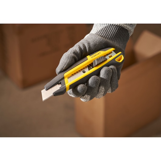 STANLEY STHT10501-0 stanleymes in een handschoenhand, geel-zwart lichaam, kartonnen dozen op de achtergrond.