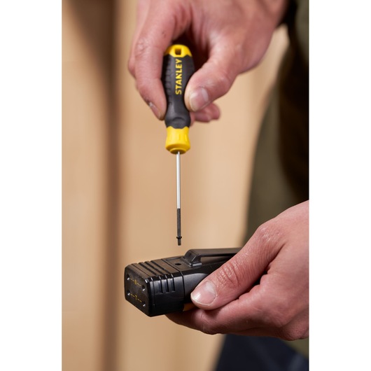 Foto van STANLEY STHT16151-0 schroevendraaier met geel-zwart handvat in gebruik op een zwart elektronisch apparaat in de hand.
