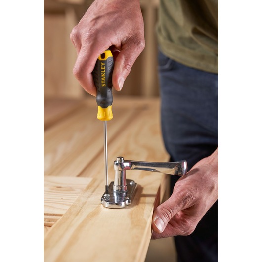 STANLEY STHT16195-0 tournevis à manche noir et jaune utilisé pour fixer une charnière sur une surface en bois.