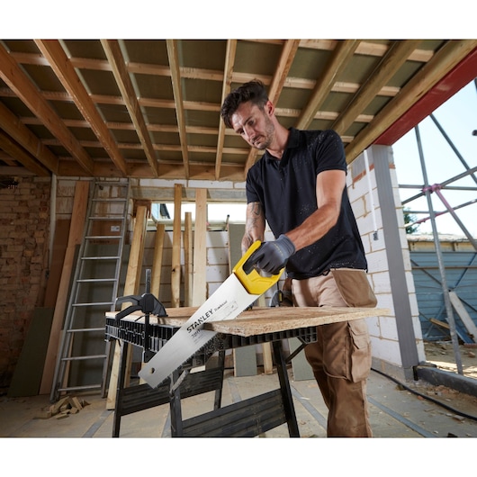 STANLEY STHT20348-1 handzaag met gele handgreep zaagt houten plank op bouwplaats.