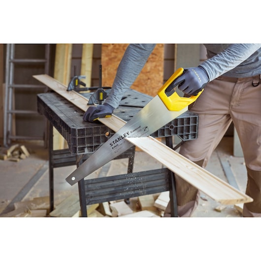 STANLEY STHT20350-1 handzaag met gele handgreep zaagt een houten plank in werkplaats, fotografie categorie.
