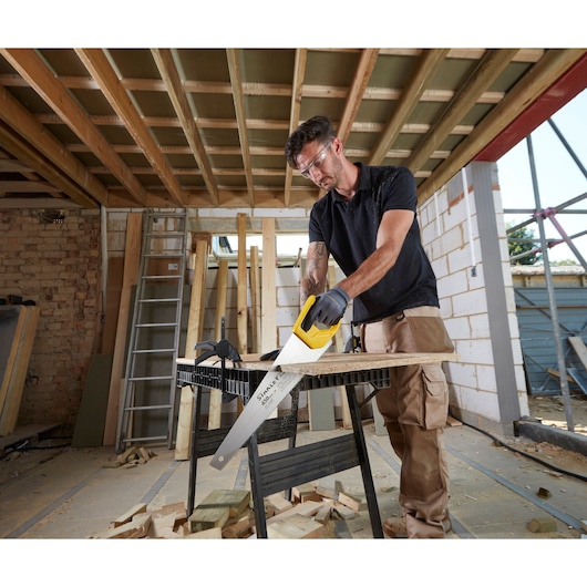 STANLEY STHT20354-1 scie à main avec manche jaune utilisée pour couper du bois sur un chantier.