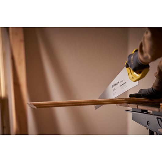 Photographie de STANLEY STHT20371-1 scie à main coupant du bois, poignée jaune et main gantée, atelier intérieur.