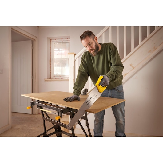 Stanley STHT20371-1 scie à main avec poignée jaune utilisée pour découper du bois sur un établi en intérieur.