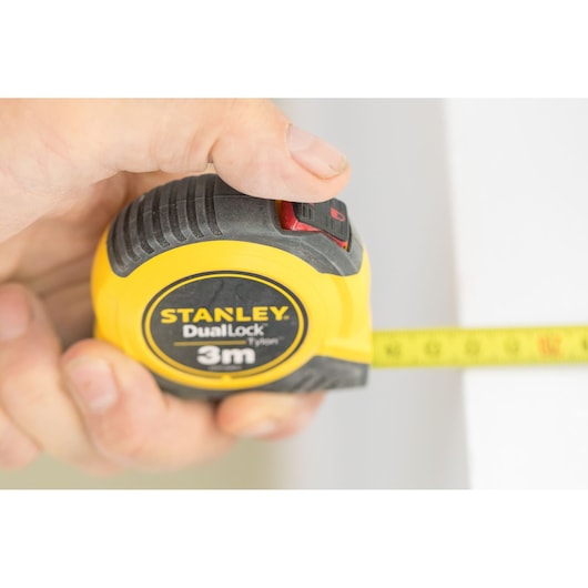 Foto van STANLEY STHT36802-0 rolmaat DualLock 3m gele behuizing in hand, band uitgetrokken.