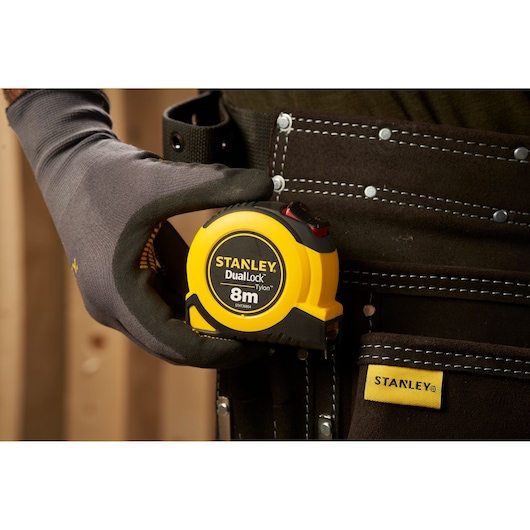 Foto van STANLEY STHT36804-0 DualLock 8m rolmaat in gereedschapsriem, vastgehouden door gehandschoende hand.