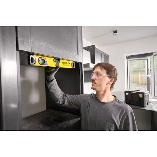 Iemand gebruikt een gele STANLEY waterpas om de uitlijning van een kast in een moderne keuken in aanbouw te controleren.