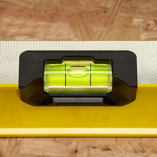 Close-up van een Stanley waterpas met een geel lichaam en een groene libel, geplaatst op een houten oppervlak.