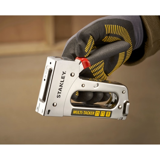 Stanley STHT6-70410 multi-tacker nietmachine vastgehouden in handschoen, close-up zijaanzicht.