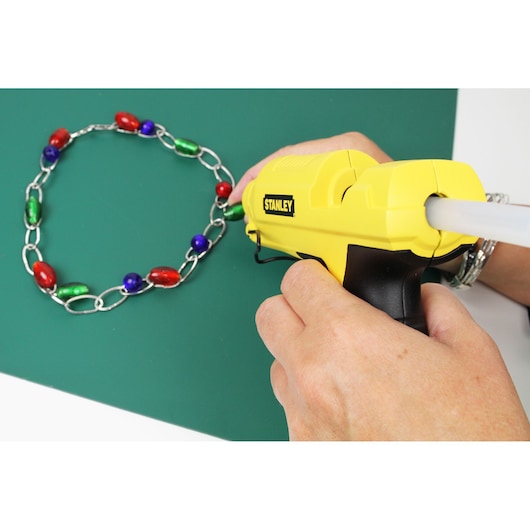 STANLEY STHT6-70417 gele lijmpistool gebruikt voor het maken van een kleurrijke kralenketting op een groen oppervlak.