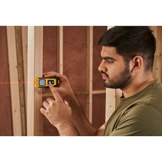 Télémètre laser STANLEY STHT77065-0 en utilisation, affichage visible et faisceau laser rouge sur un chantier.