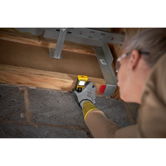 STANLEY STHT77065-0 détecteur de montants utilisé sur poutre en bois, gros plan, utilisateur avec gants.
